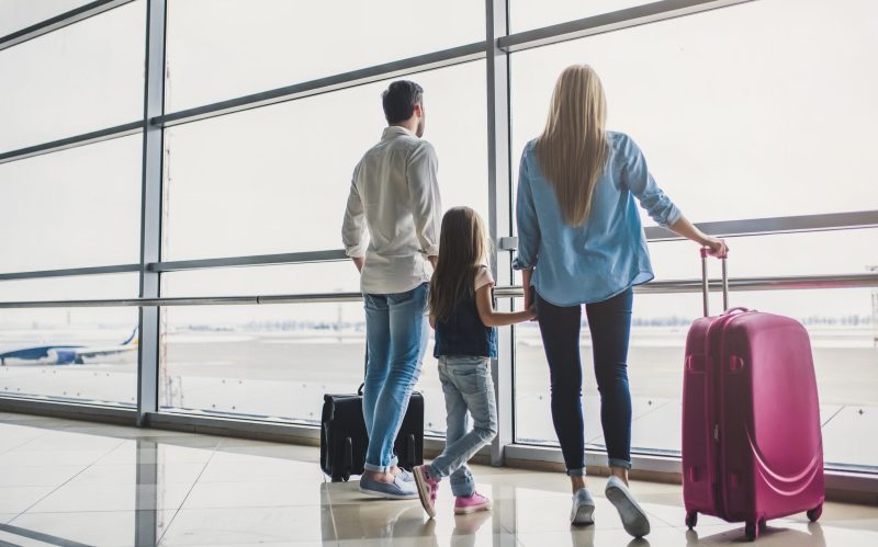 A family with young kids happily walking through an airport with suitcases.