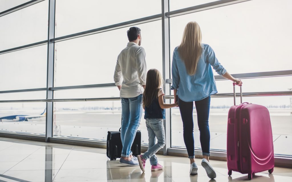 A family with young kids happily walking through an airport with suitcases.